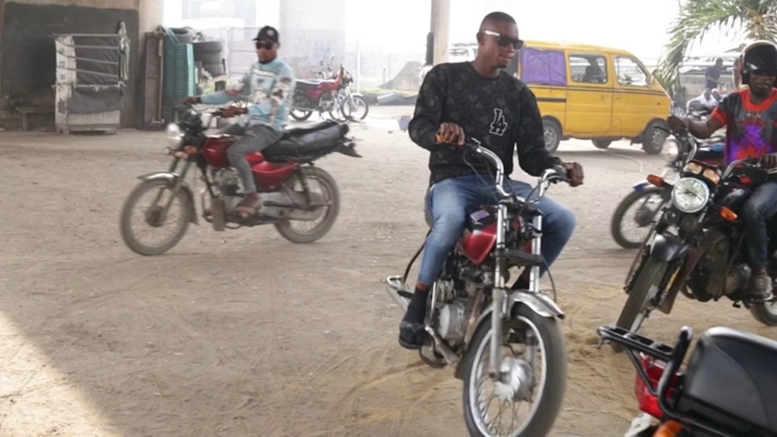 A group of men wearing sunglasses and riding motorcycles in the dusty streets of Nigeria.