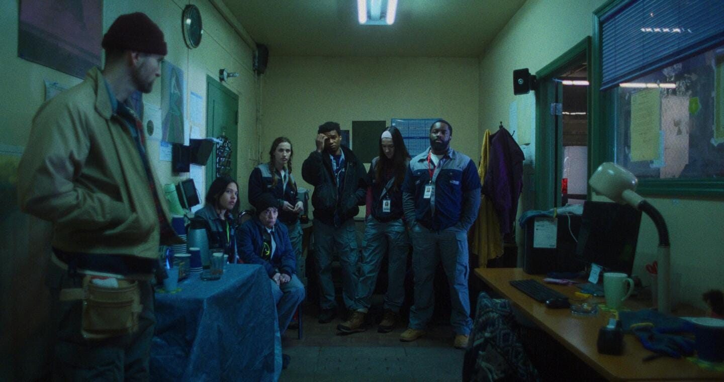 A group of workers sitting in a factory office, preparing for a meeting.