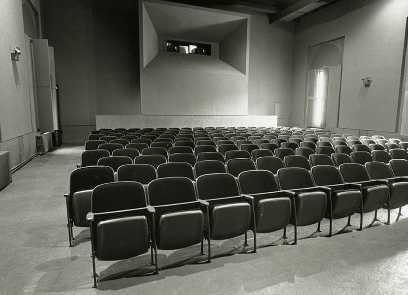 Black and white image of a cinema screening hall, with empty rows of seats and clean walls.
