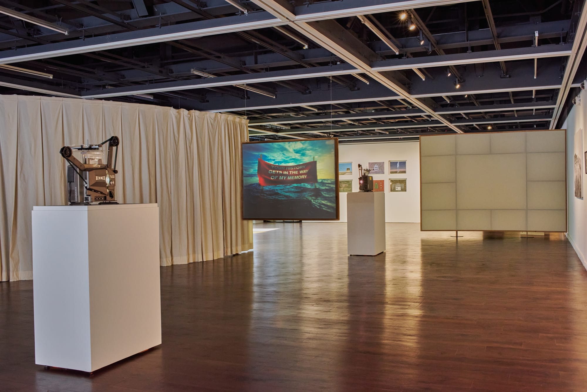 A gallery floor with an installation comprising two 16mm film projectors and a screen hanging between them.