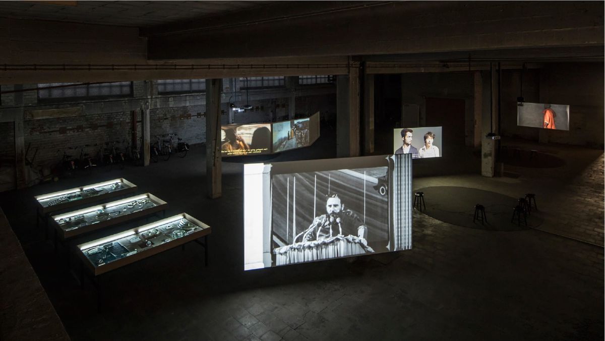 A high-angle view of a darkened gallery with multiple moving image installations.