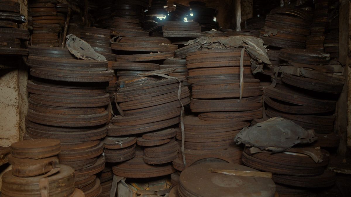 Stacks of old, rusted film cans and decaying reels of film in a dark and dusty archive. 
