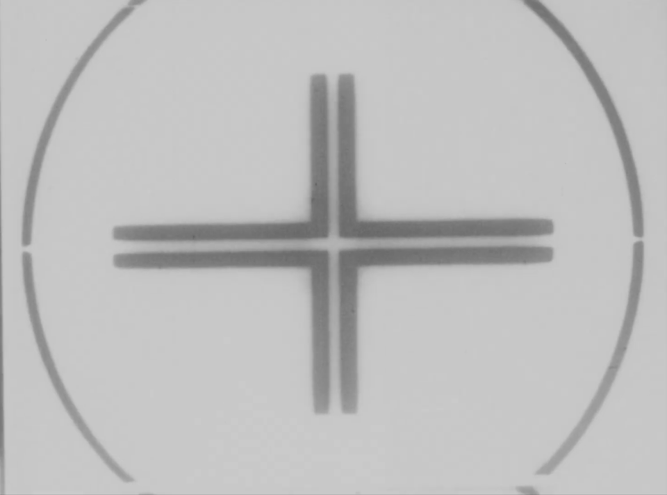 A black and white film frame with technical markings, a cross in the center of a circle.