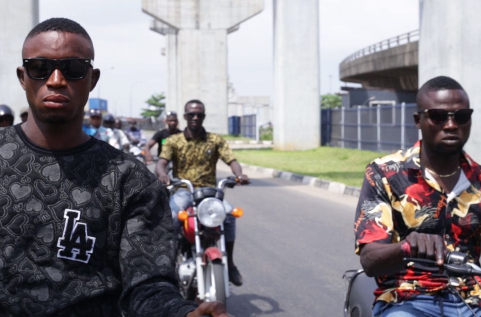 A group of young Black men in sunglasses riding motorcycles in the city streets.