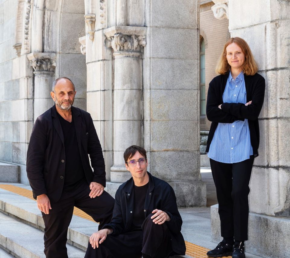 Three individuals dressed in black posing for a portrait on the steps of an ornate building.