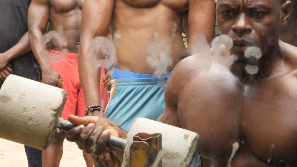 Three African men with their shirts off looking into a mirror while they work out with homemade weights.