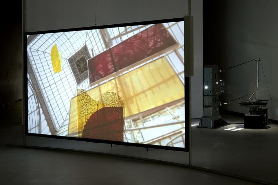 A translucent screen with colorful shapes projected on it, and behind it a modified analog film projector.
