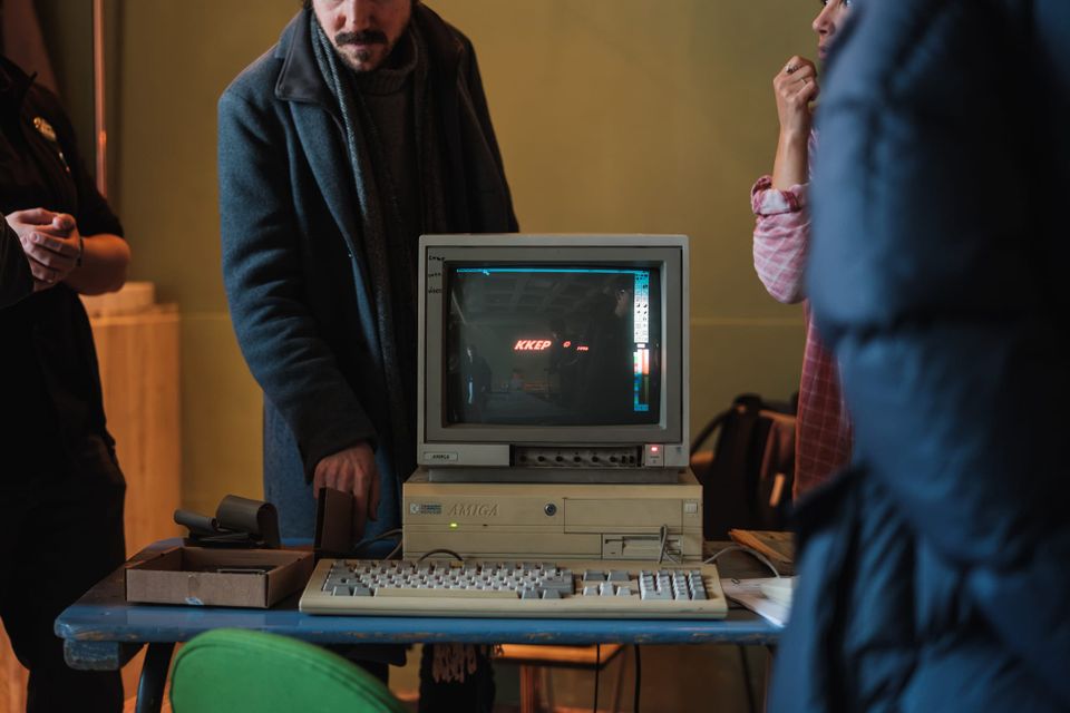 An Amiga desktop computer from the 1980s sits on a table while people gathered around examine it.