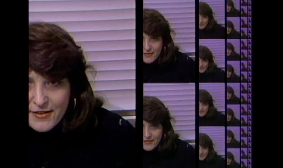 A woman with long brown hair and a dark shirt framed in a lo-fi video image that repeats in successively smaller sizes into infinity.