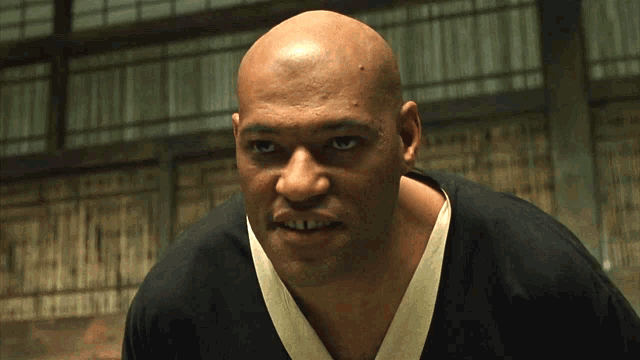 Morpheus and Neo in the white dojo, mid-spar. Neo swings. Morpheus deflects. Morpheus never lands the finishing move.