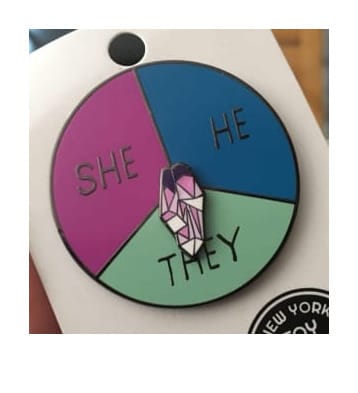 a genderfluid pronoun pin with a spinner that can point to she, he, or they