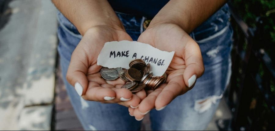 Photo of manicured hands offering a bunch of US coins along with a paper scrap that reads "make a change"