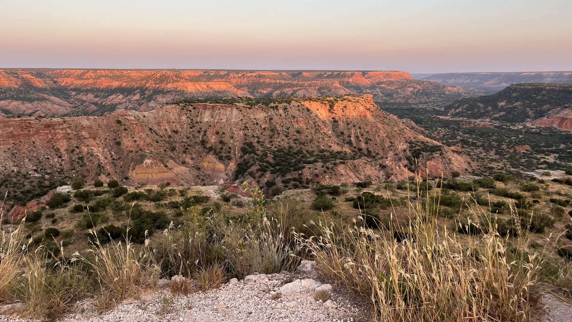View of Palo Duro Canyon from the rim looking down into the canyon as sunset highlights the orange canyon walls.