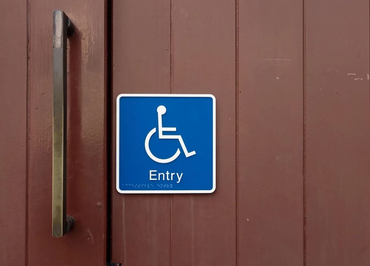 White on blue wheelchair symbol sign labeled "Entry" on a brown painted door
