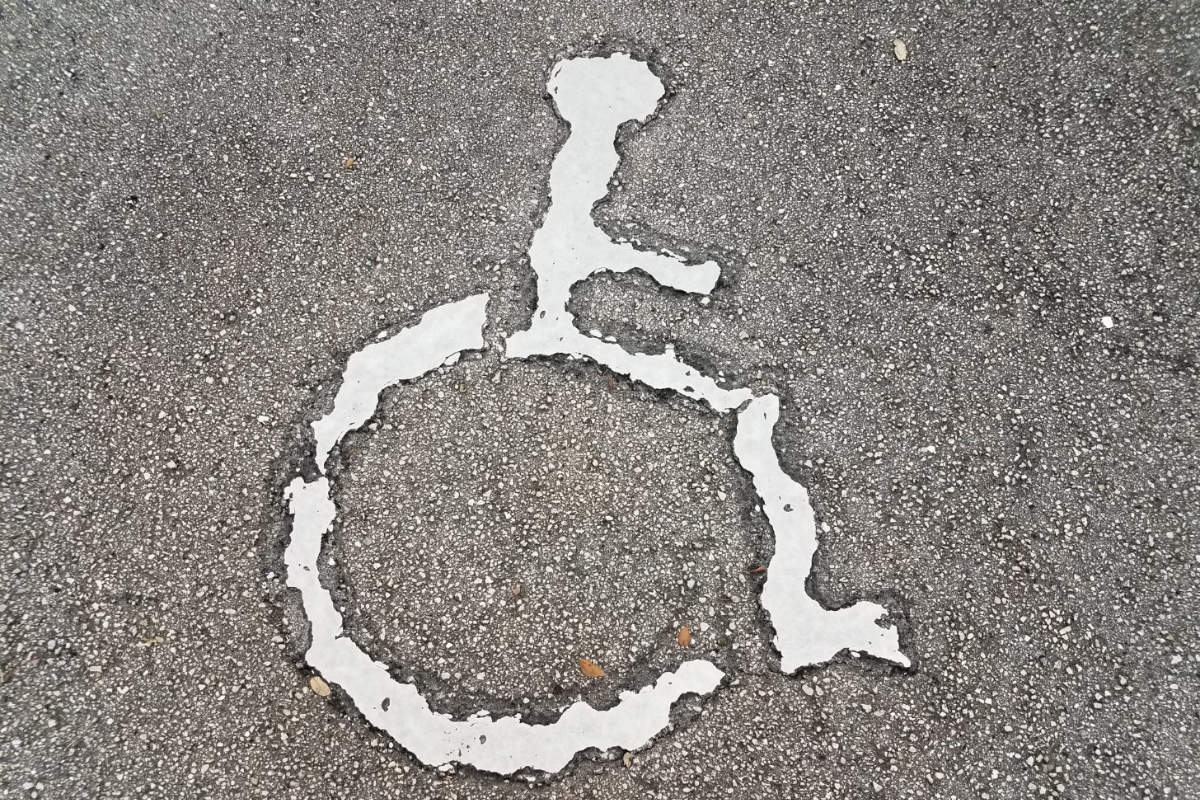 White peeling and eroded wheelchair symbol painted on gray pavement