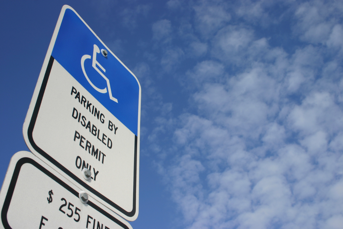Parking by disabled permit only sign with white on blue wheelhair symbol against a blue sky with fluffy clouds