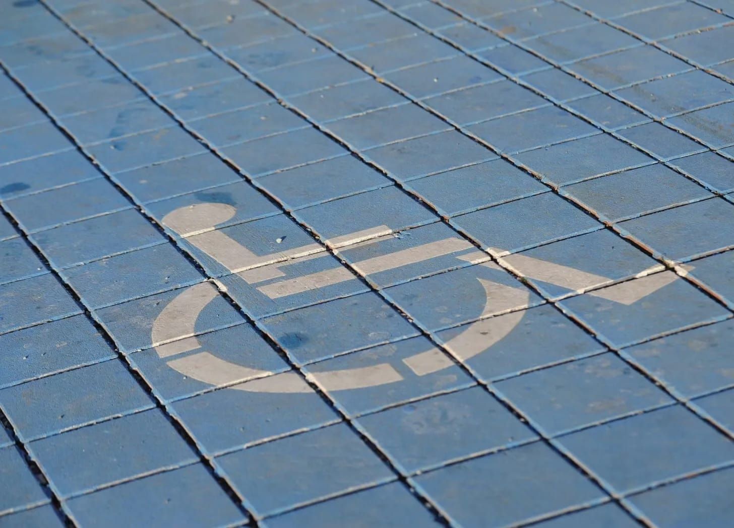 White wheelchair symbol stenciled onto blue square tiled pavement