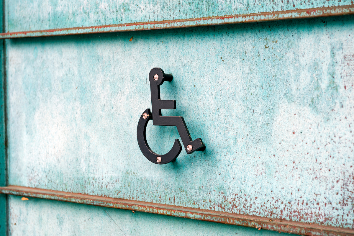 Metal wheelchair symbol rivited onto a rust-flecked metal wall