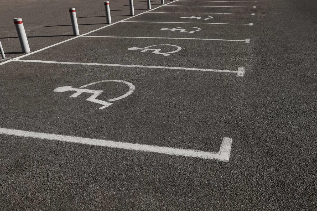 Row of accessible parking spaces marked on pavement by white lines and wheelchair symbols