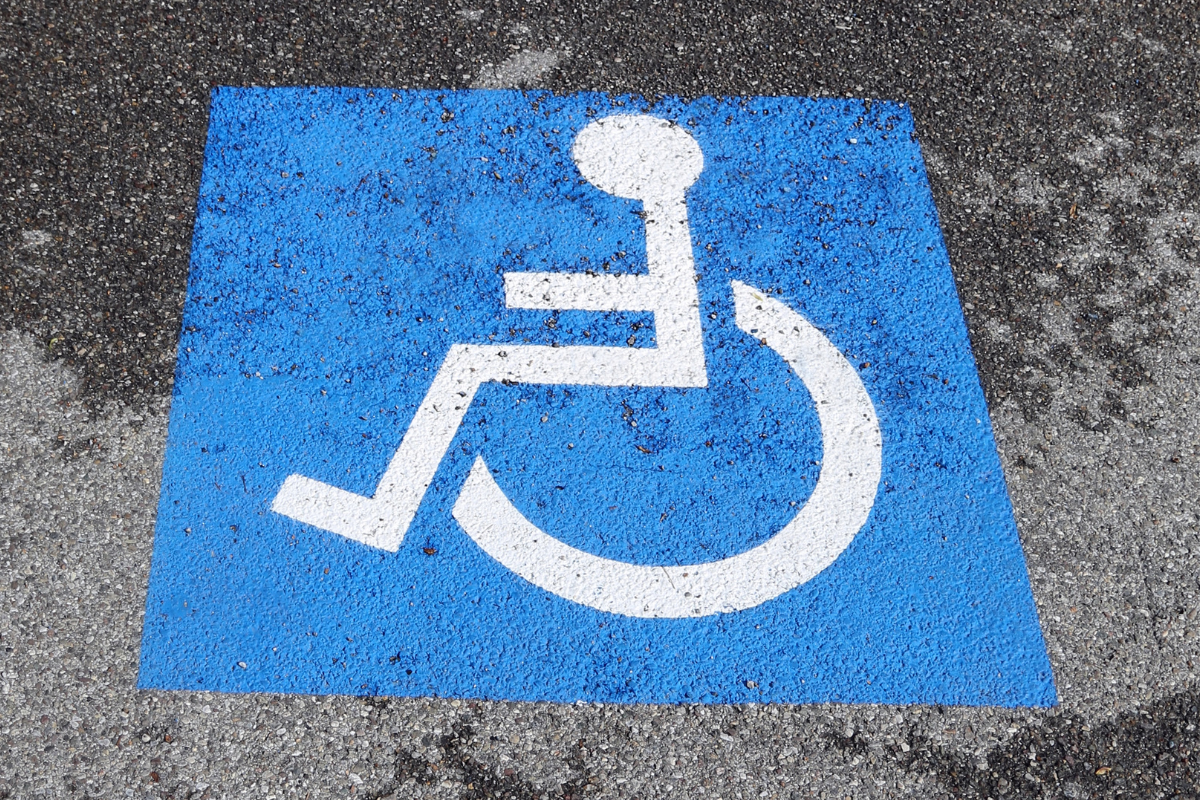 White on blue wheelchair symbol painted on rough grey pavement