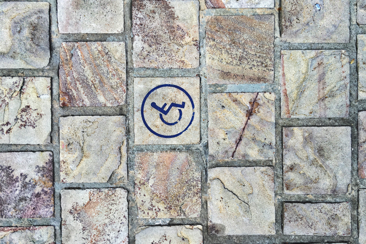 Blue wheelchair symbol in a circle painted onto a textured brick wall
