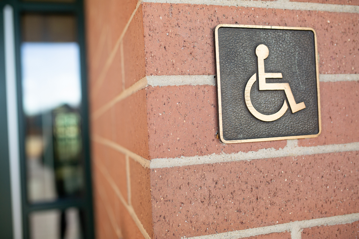 Gold colored wheelchair symbol on a black metal sign mounted on a brick wall