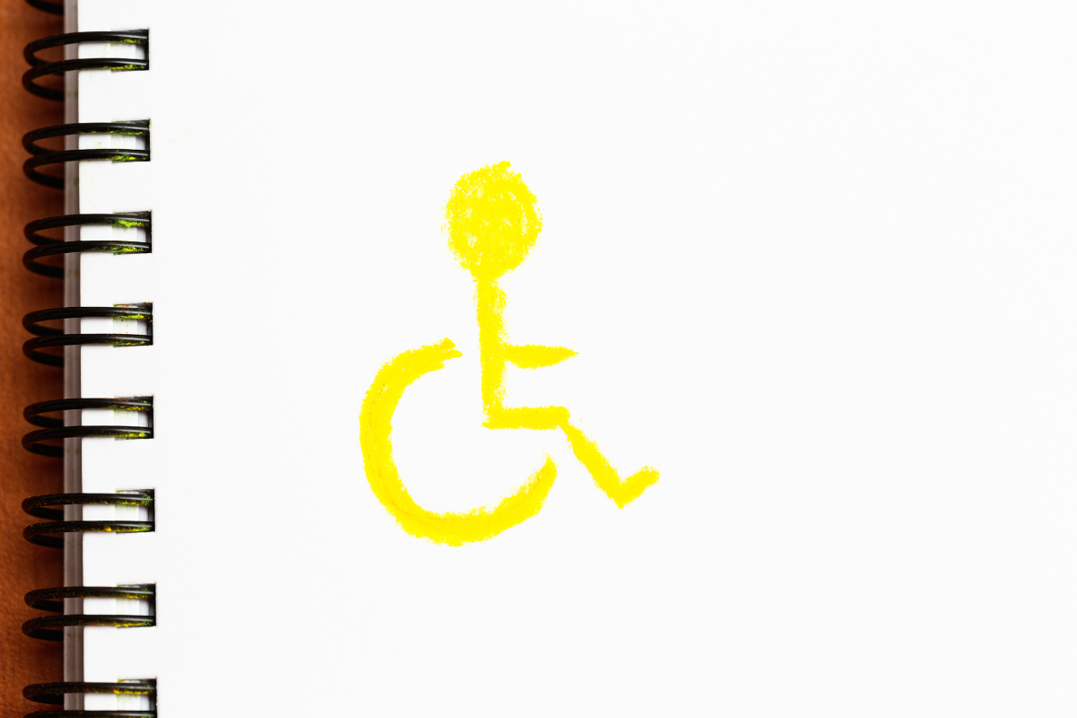 Yellow sketched wheelchair symbol on a spiral notebook page of white paper