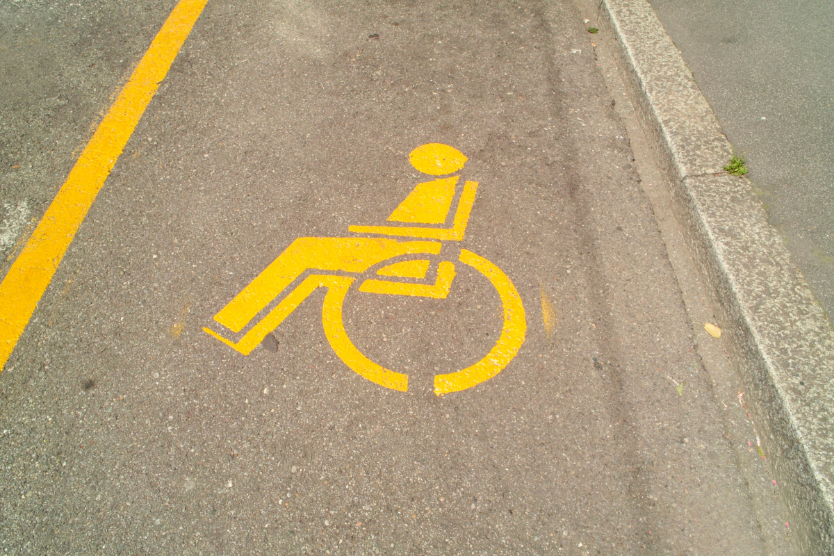 Yellow wheelchair symbol stenciled on tan pavement marking accessible parking space