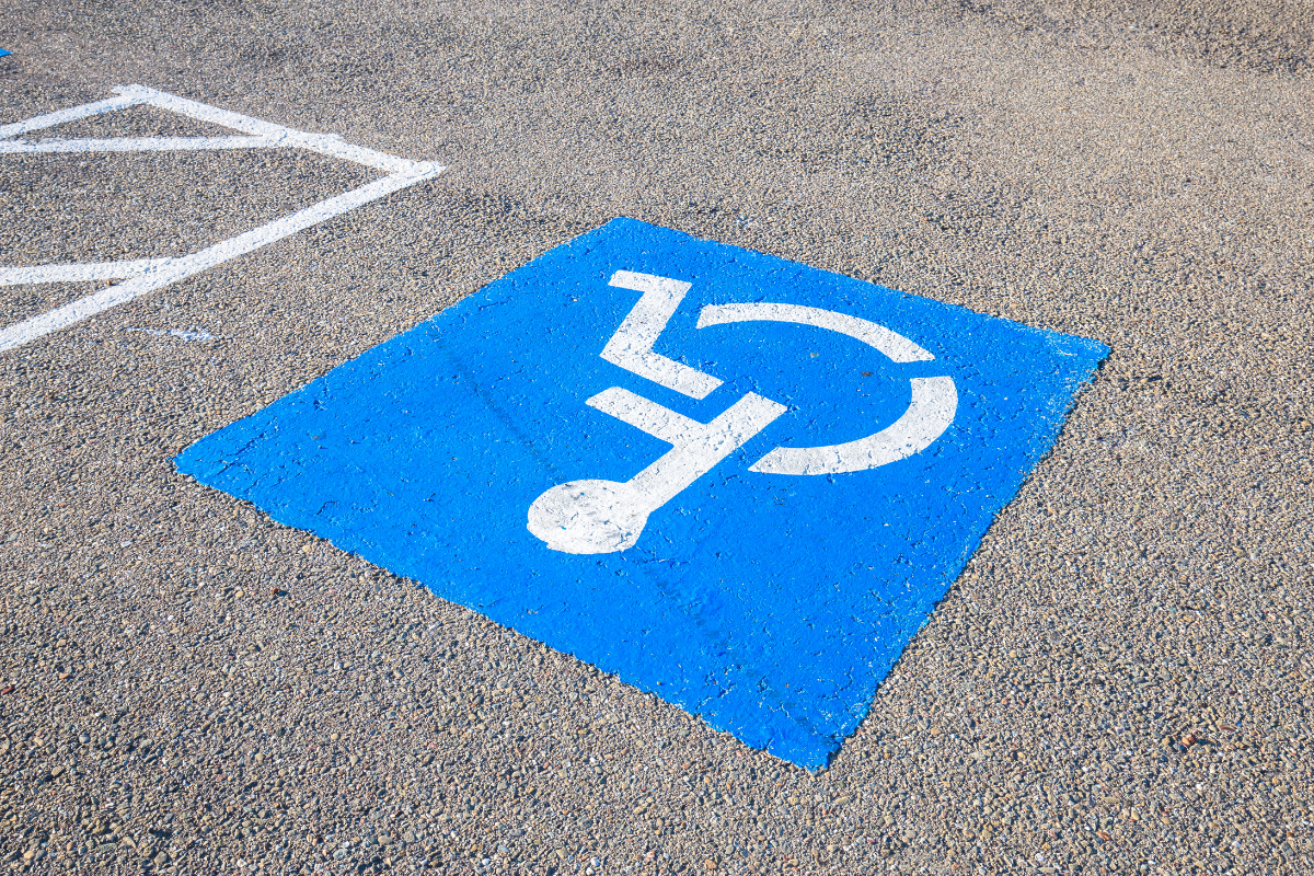 Upside down view of white on blue wheelchair symbol painted on grey pavement of accessible parking space