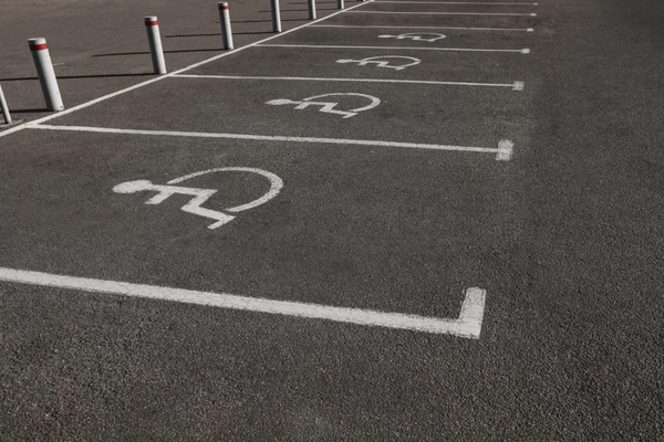 Photo of a row of four accessible parking spaces, marked on black pavemenet with white lines and wheelchair symbols