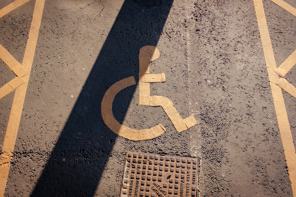Slightly peeling yellow wheelchair symbol on brown pavement marking accessible parking space