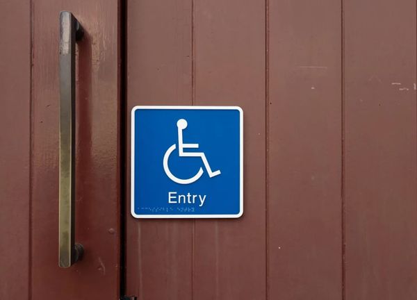 White on blue wheelchair symbol marked Entry mounted on a wooden door