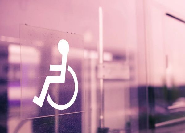 White wheelchair symbol sign on a rose tinted glass wall