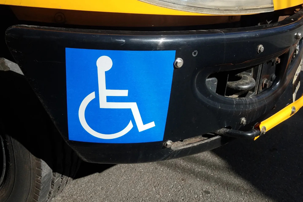 White on blue square wheelchair symbol bumper sticker on black painted car bumper