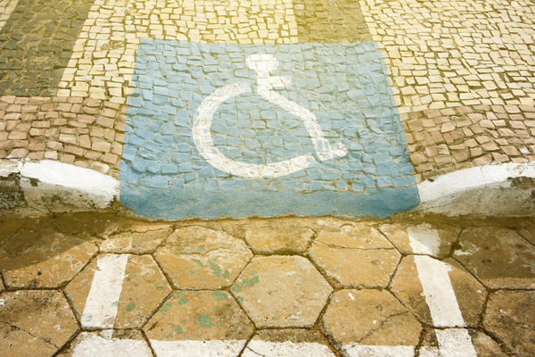 White on blue wheelchair symbol in faded paint on uneven paving stone curb ram
