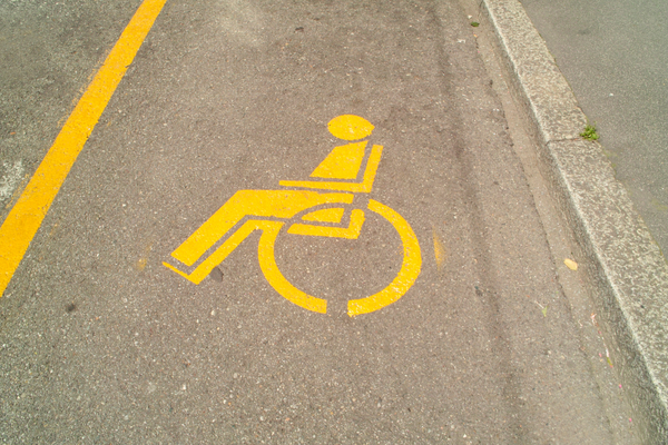 Yellow wheelchair symbol stenciled on tan pavement marking accessible parking space