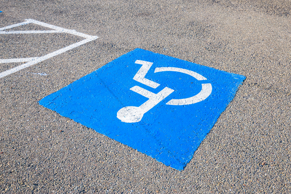 Upside down view of white on blue wheelchair symbol painted on grey pavement of accessible parking space