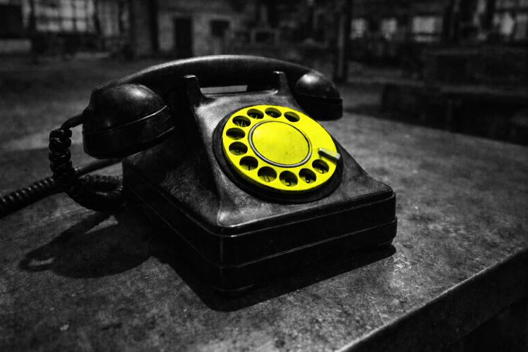 Vintage black rotary telephone on a worn surface, with a bright yellow dial in focus against a blurred industrial background