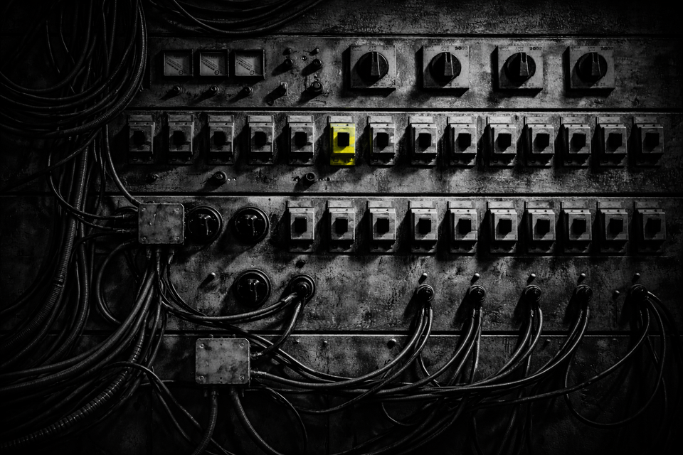 Black-and-white industrial control panel with rows of switches and cables; one central switch stands out in vivid acid yellow under harsh side lighting