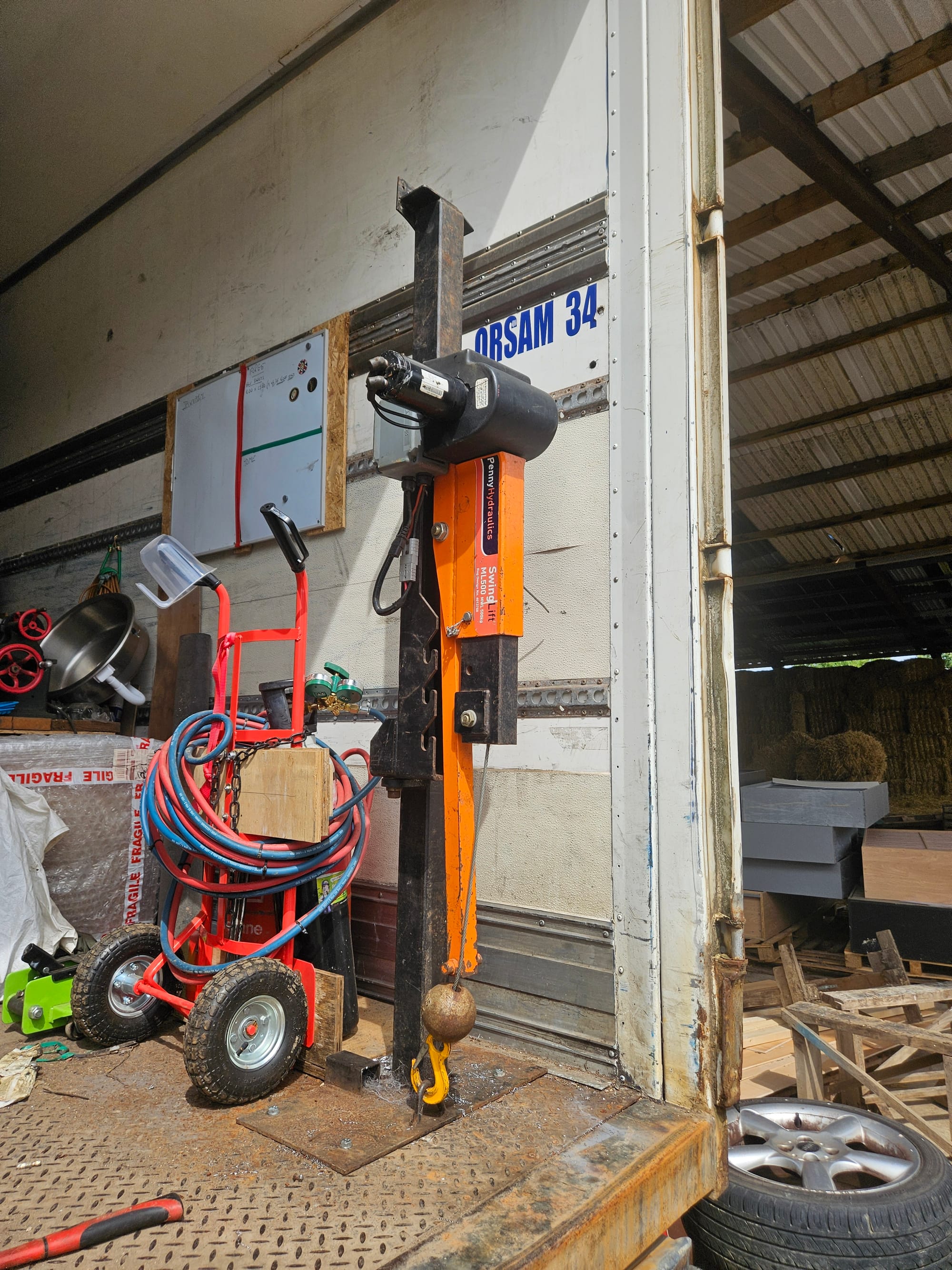 An orange crane lift is bolted to the floor of a trailer