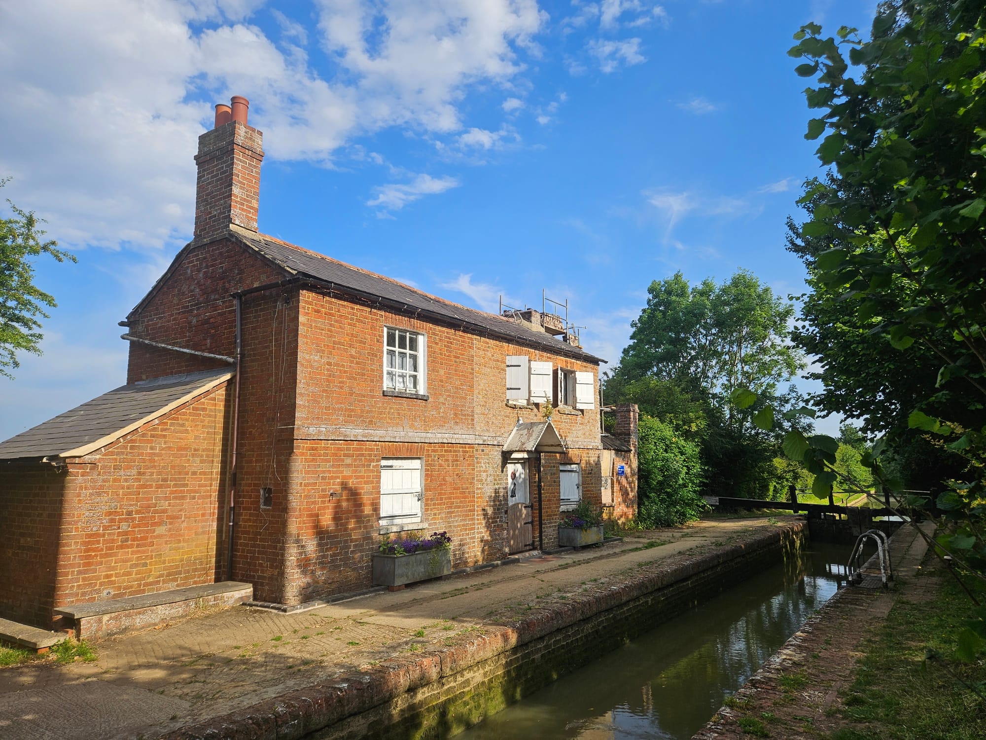 A 19th Century brick built cottage stands next to a canal lock filled with water 