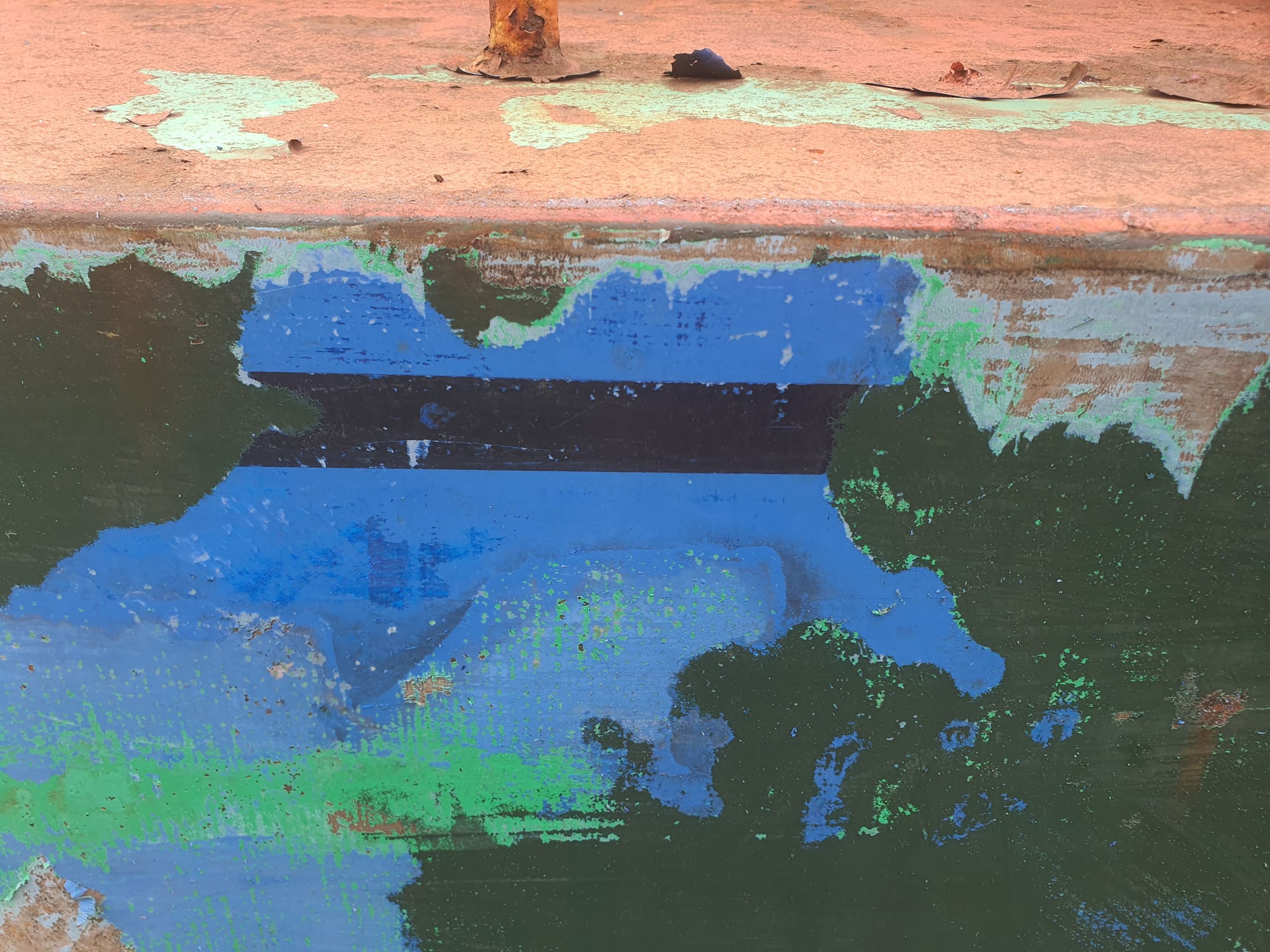 A small section of painted hull showing a mix of blues and greens, with sky blue and a navy stripe through it