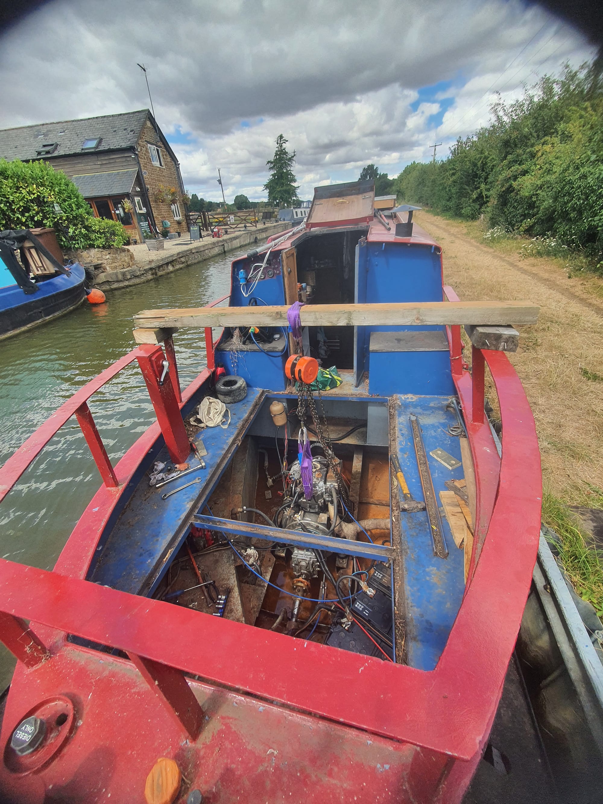 An image of the rear deck of a red narrowboat, with the engine suspended on a makeshift hoist