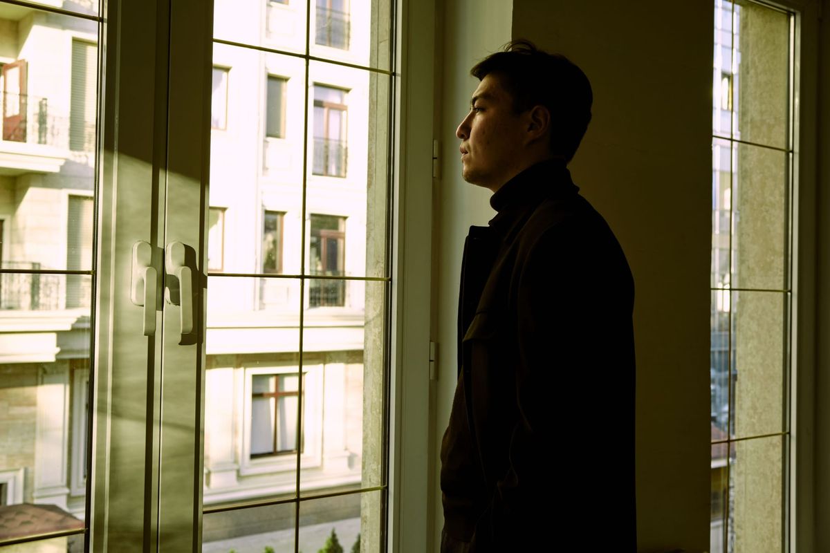 Person reflecting while looking through a window after moving to a new country.