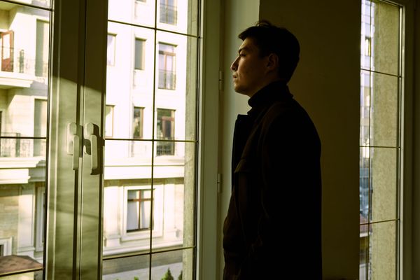 Person reflecting while looking through a window after moving to a new country.
