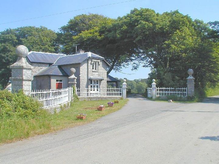 A gray stone house with a white fence around it and tall trees. 