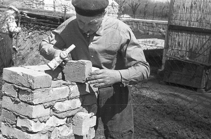 A black and white photo of an old man laying bricks.