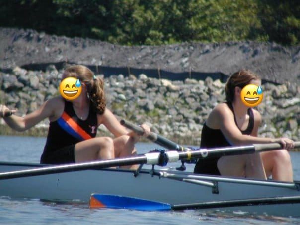 Two white women in a rowing shell in black unis holding orange and blue oars.