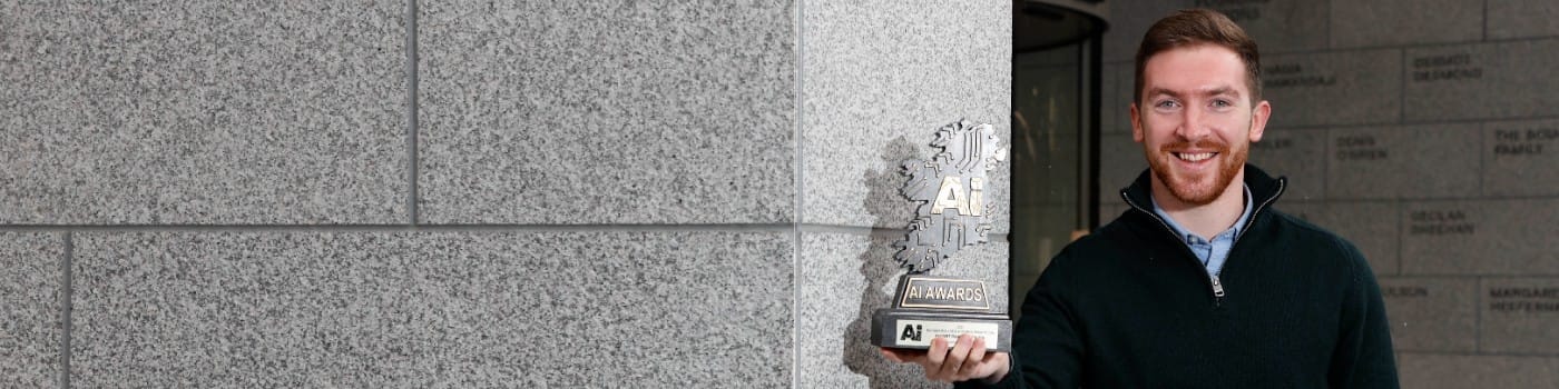 A smiling man holds up an award that's shaped like Ireland with 'AI' stamped on it.