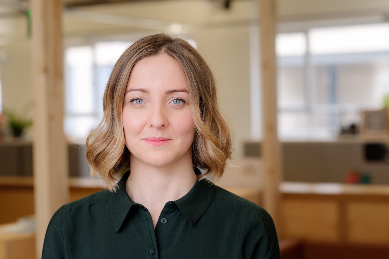 A headshot of a blonde woman in a dark shirt in an office.